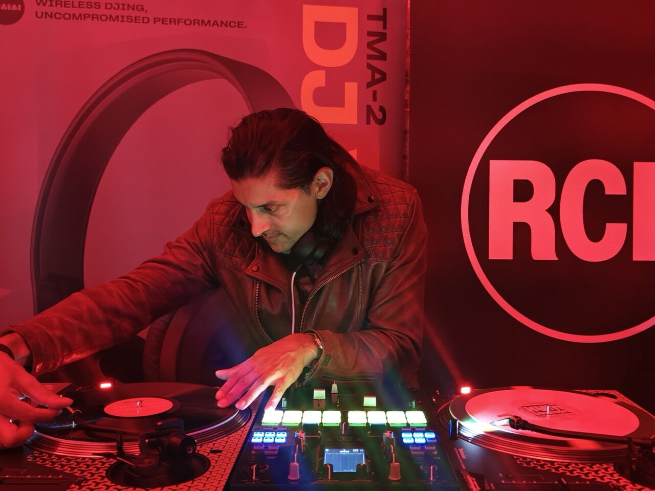 DJ SR scratching on turntables in a red-lit DJ booth