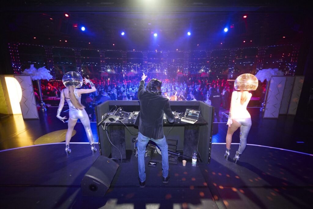 DJ SR with a hand in the air between two disco ball dancers at a corporate gala in Monte Carlo