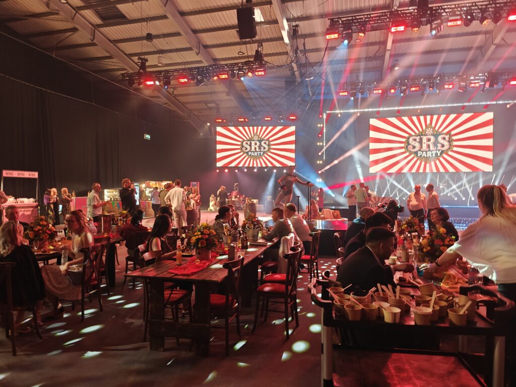 SRS Party 2025: guests at long tables with the SRS Party logo on the stage screens